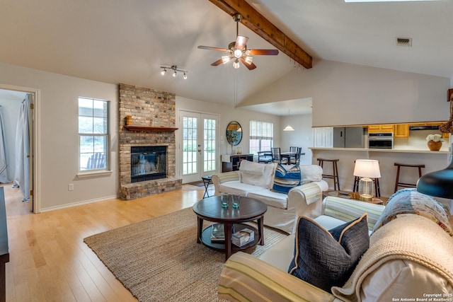 living room featuring lofted ceiling with beams, a fireplace, light wood-style floors, a ceiling fan, and visible vents