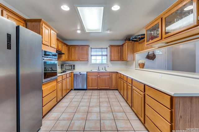 kitchen featuring appliances with stainless steel finishes, a sink, light countertops, a peninsula, and light tile patterned floors