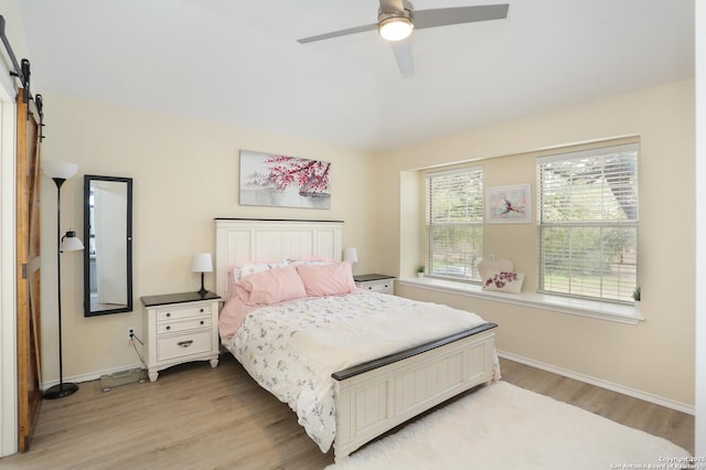 bedroom featuring a ceiling fan, baseboards, a barn door, and light wood-style floors