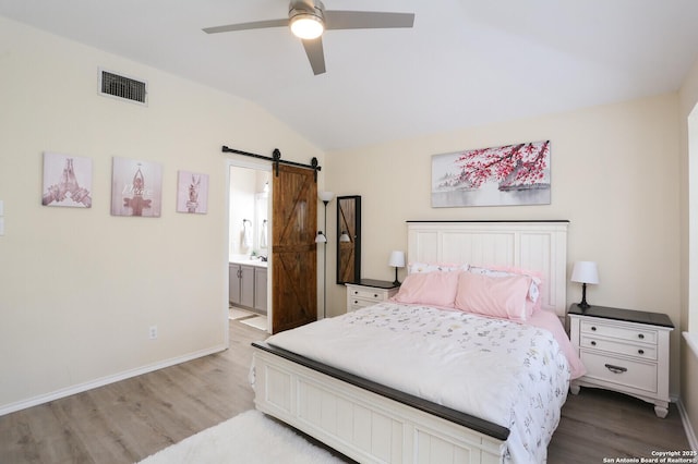 bedroom with visible vents, vaulted ceiling, a barn door, wood finished floors, and baseboards