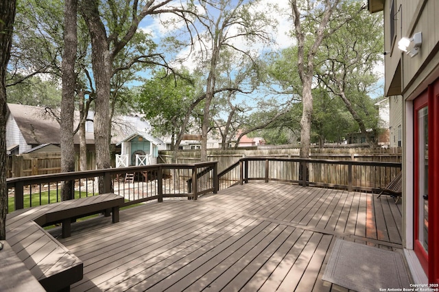 wooden terrace featuring an outdoor structure, a fenced backyard, and a storage unit