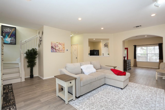 living area featuring visible vents, arched walkways, stairs, light wood-style floors, and recessed lighting