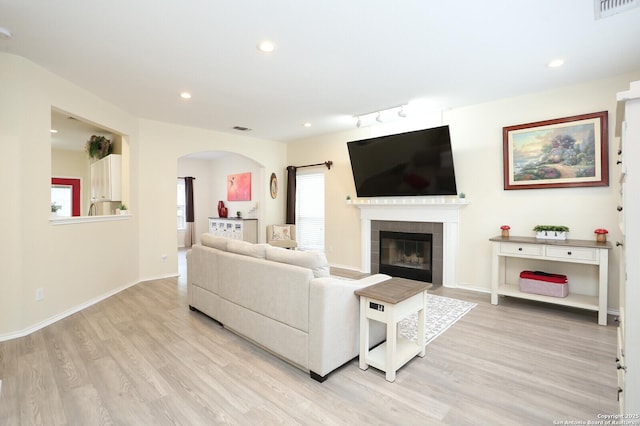 living room with rail lighting, arched walkways, light wood finished floors, and visible vents