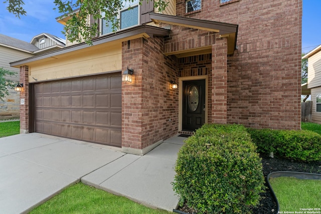 view of exterior entry featuring brick siding, an attached garage, and driveway