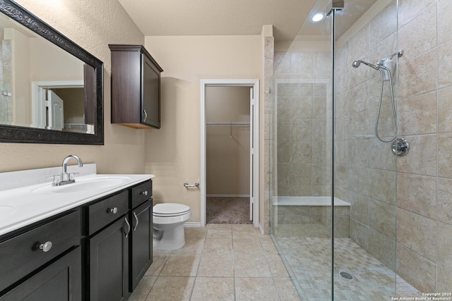 bathroom with vanity, toilet, baseboards, tiled shower, and a spacious closet