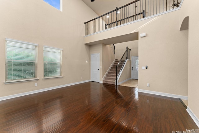 unfurnished living room featuring baseboards, wood finished floors, stairway, and a towering ceiling