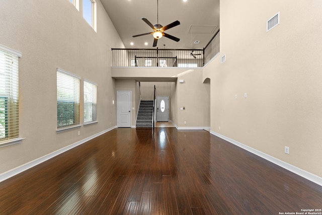 unfurnished living room with stairs, a ceiling fan, wood finished floors, a towering ceiling, and visible vents