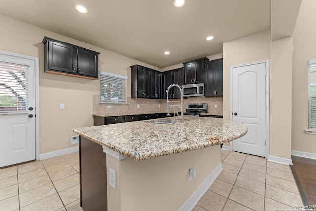 kitchen with dark cabinets, light stone counters, backsplash, and stainless steel appliances