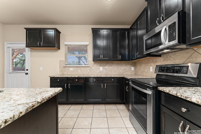kitchen with dark cabinetry, decorative backsplash, light stone counters, and stainless steel appliances