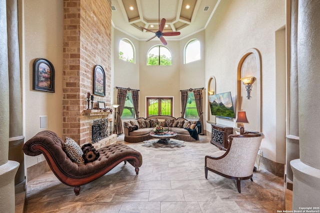 interior space with crown molding, ceiling fan, a brick fireplace, a towering ceiling, and coffered ceiling