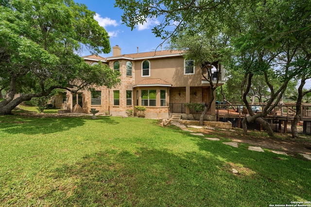 back of house with brick siding, stucco siding, a chimney, a balcony, and a lawn
