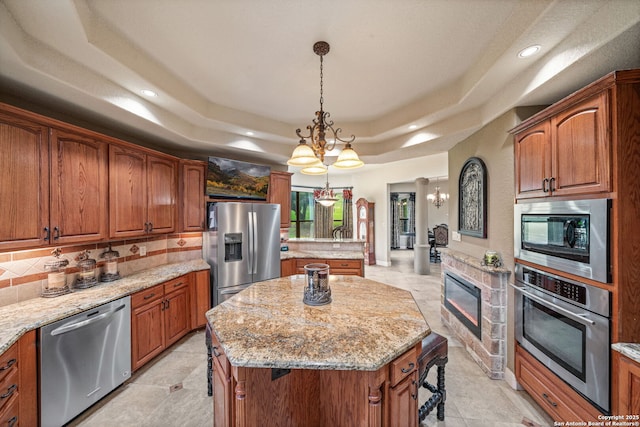 kitchen with a chandelier, a center island, stainless steel appliances, tasteful backsplash, and a tray ceiling