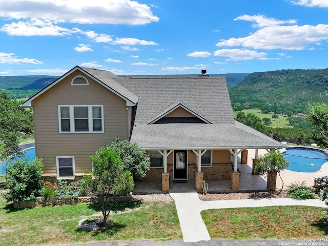 view of front of home with covered porch, a mountain view, roof with shingles, and a front lawn