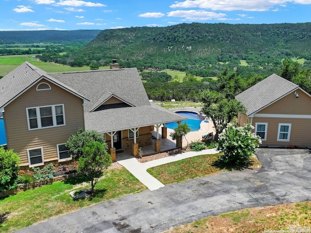 view of front of house featuring roof with shingles, a chimney, a porch, a mountain view, and a forest view