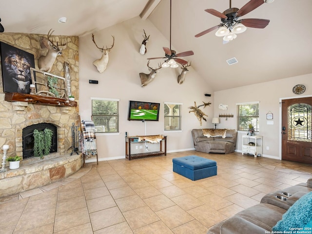 tiled living room with ceiling fan, high vaulted ceiling, a stone fireplace, baseboards, and visible vents