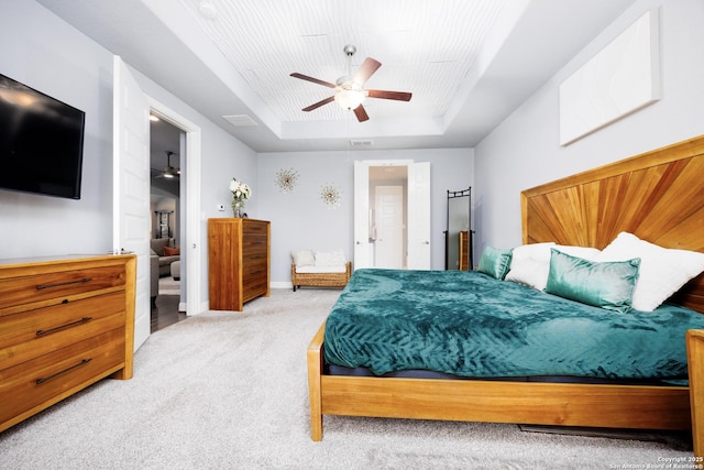 carpeted bedroom with a ceiling fan, a tray ceiling, and visible vents