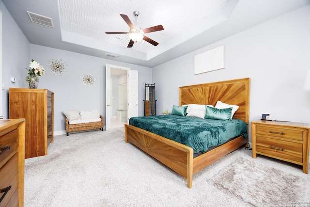 bedroom with a tray ceiling, light colored carpet, ceiling fan, and visible vents