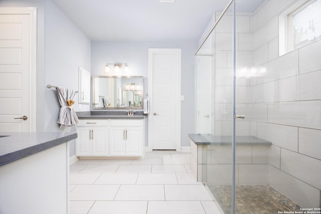 bathroom with vanity, tile patterned flooring, baseboards, and a tile shower