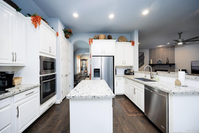 kitchen with ceiling fan, appliances with stainless steel finishes, a center island, arched walkways, and a sink