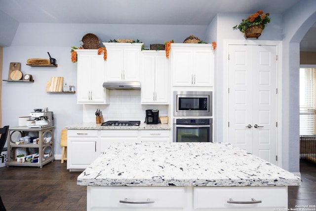kitchen featuring appliances with stainless steel finishes, under cabinet range hood, arched walkways, and white cabinetry