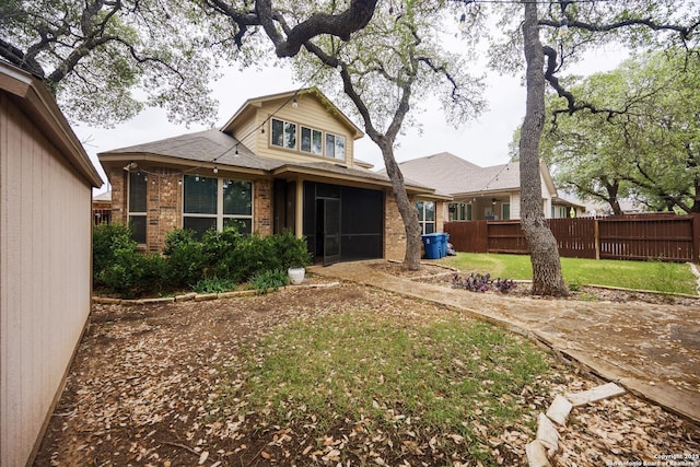 back of property featuring a yard, brick siding, fence, and a sunroom