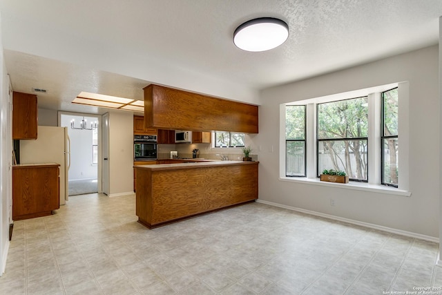19750 Encino Way, San Antonio, TX 78259 - kitchen with white appliances, brown cabinets, a peninsula, baseboards, and a textured ceiling