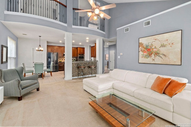 living room featuring visible vents, a towering ceiling, ceiling fan with notable chandelier, and light colored carpet