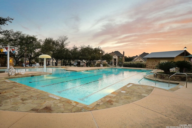 pool at dusk with a community pool and a patio