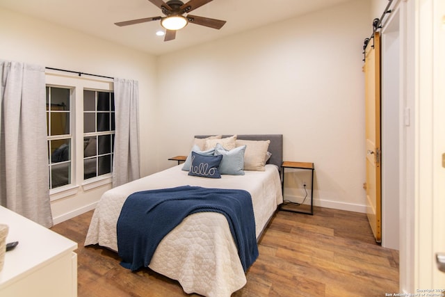 bedroom with a barn door, recessed lighting, baseboards, a ceiling fan, and wood finished floors