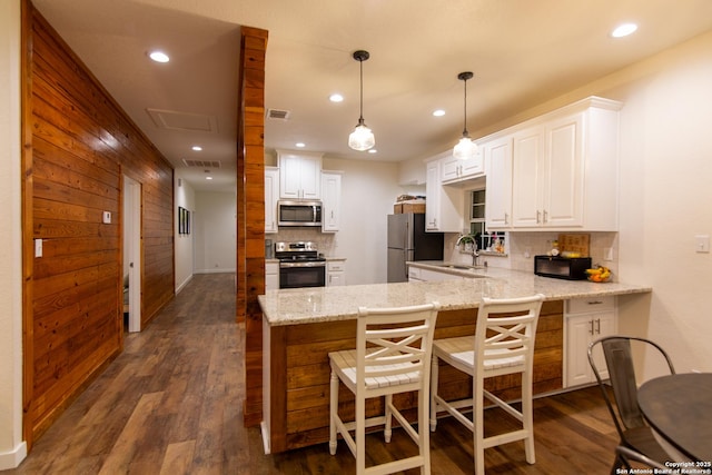 kitchen featuring decorative backsplash, appliances with stainless steel finishes, a sink, a peninsula, and white cabinetry