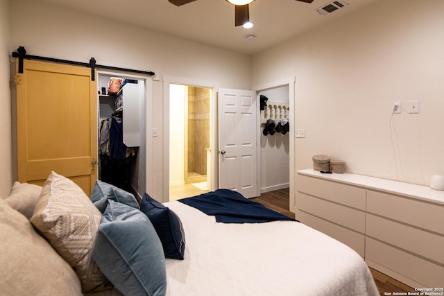 bedroom featuring wood finished floors, visible vents, a walk in closet, and ensuite bath