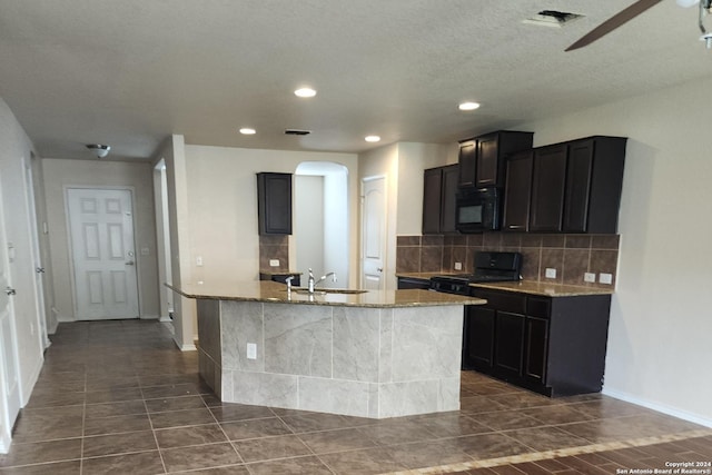kitchen with a kitchen island with sink, light stone countertops, a sink, backsplash, and black appliances