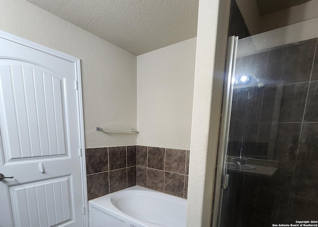 full bathroom featuring a textured ceiling, a bath, and a stall shower