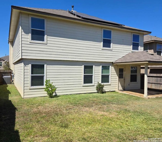 back of property with solar panels, a lawn, a patio area, central air condition unit, and fence
