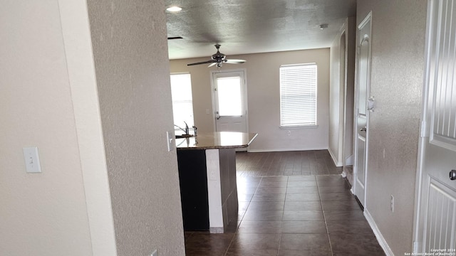 interior space featuring baseboards, a textured ceiling, a textured wall, and dark tile patterned flooring