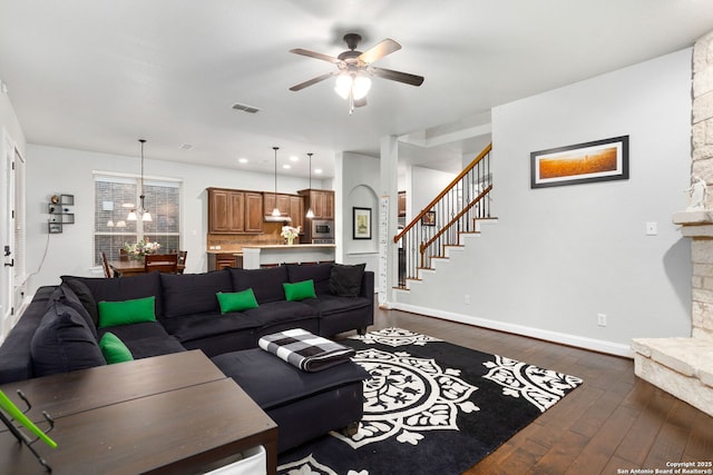living area featuring stairs, a ceiling fan, baseboards, visible vents, and dark wood-style floors