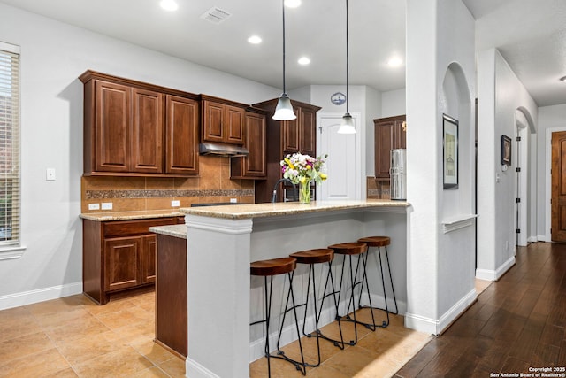 kitchen featuring a kitchen breakfast bar, decorative light fixtures, baseboards, tasteful backsplash, and visible vents