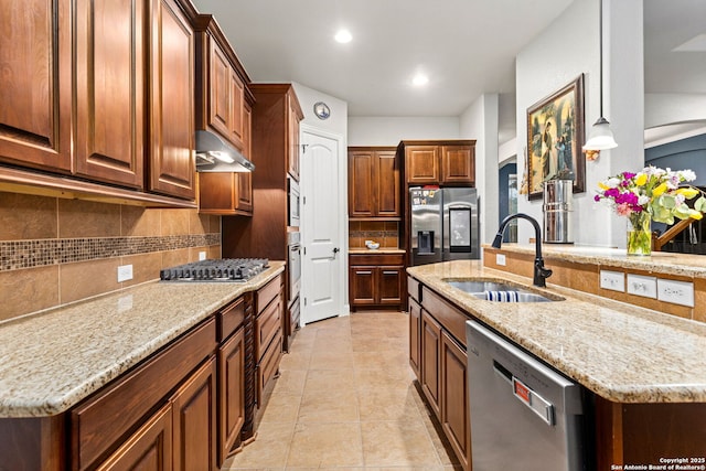 kitchen with light stone countertops, under cabinet range hood, a sink, backsplash, and stainless steel appliances