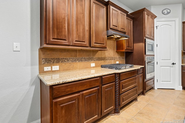 kitchen with a textured wall, light stone countertops, appliances with stainless steel finishes, decorative backsplash, and under cabinet range hood