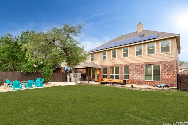 rear view of property with brick siding, an outdoor living space with a fire pit, roof mounted solar panels, a fenced backyard, and a patio