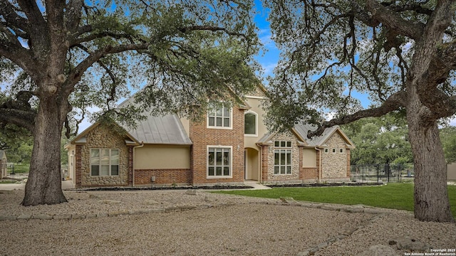 traditional-style house with a standing seam roof, metal roof, fence, a front lawn, and stone siding