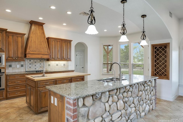 kitchen with visible vents, custom exhaust hood, an island with sink, arched walkways, and a sink