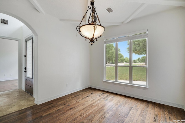spare room with baseboards, arched walkways, beam ceiling, and wood finished floors