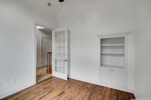 spare room with high vaulted ceiling, built in shelves, french doors, baseboards, and wood finished floors
