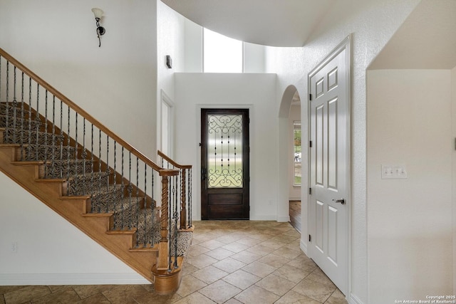 foyer with baseboards, arched walkways, a towering ceiling, and stairway