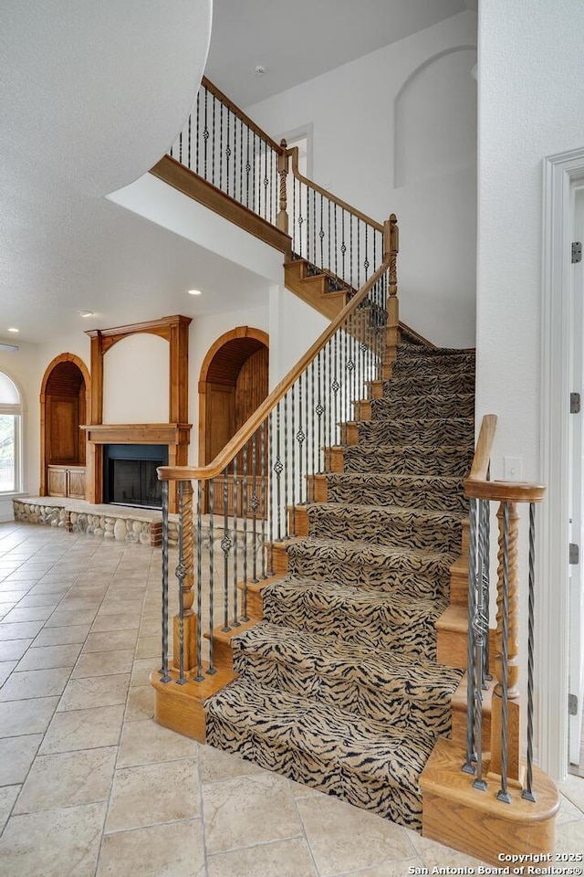 stairway featuring recessed lighting, arched walkways, a high ceiling, and a fireplace