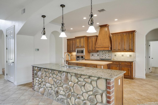 kitchen featuring visible vents, a sink, a center island with sink, arched walkways, and stainless steel appliances