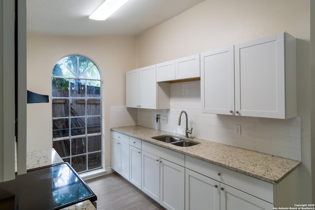kitchen featuring backsplash, range, light stone countertops, light wood-type flooring, and a sink