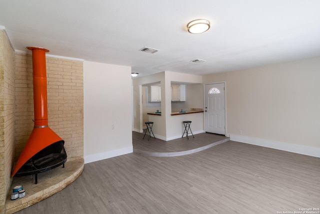 unfurnished living room with baseboards, a wood stove, wood finished floors, and visible vents