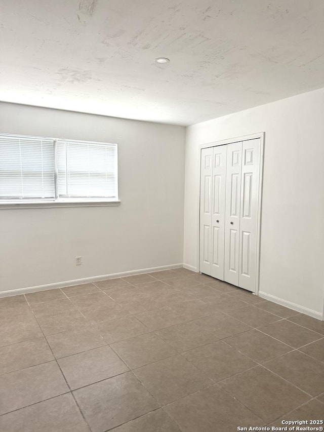unfurnished bedroom featuring baseboards, tile patterned floors, and a closet